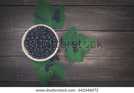 Fresh black currants bowl top view on rustic wood background. Natural organic berries with green leaves scattered on weathered grey wooden table, dark filter