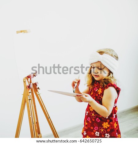 portrait of a little girl with an easel and paints, creating a painting