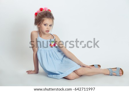 Little fashionista. Girl kid preteen in studio posing, sitting on the floor, red pink floral headband on head light blue dress looking at you camera serious isolated white background. horizontal image