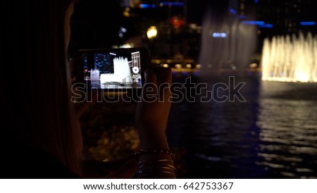 Young woman takes photos using smart mobile cell phone camera of a dancing fountain show in Las Vegas. Share pictures and video on social media with friends and family