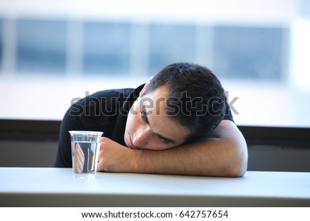 Man lying on a table and looking at plastic glass of water, Horizontal indoors shot