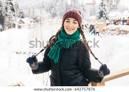 The beautiful girl walks in winter day. On her a menthol scarf, a lilac cap and a blue jacket. She holds the braid and lovely smiles.