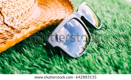 Sunglasses with the reflection of  blue sky and hat on green grass, Soft focus.
