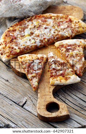 Freshly baked pizza cut into pieces on a wooden board, rustic style.