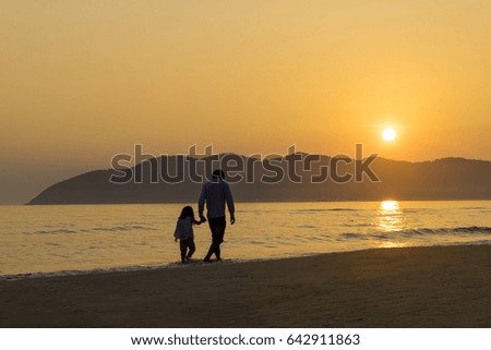 Father and daughter walking on a beach into the sunrise. 