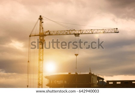 Silhouettes of a construction crane and building against a dramatic sky at sunset. Construction of buildings and structures.