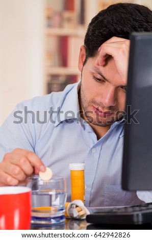 Handsome bored man drooping a pill effervescent tablet in a glass of water in his office