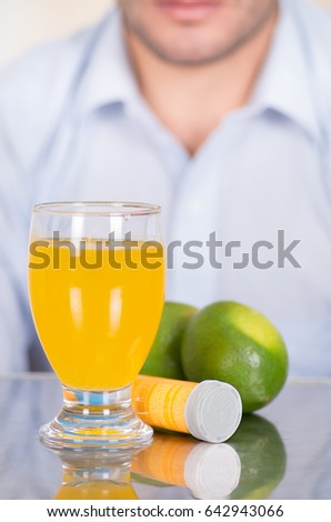 Handsome guy behind of Lemon, pills of vitamin C and a glass of vitamin C dissolved over the table