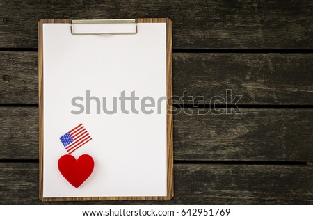 Blank white paper on wooden clipboard with red heart and American flag with space on dark vintage wooden floor