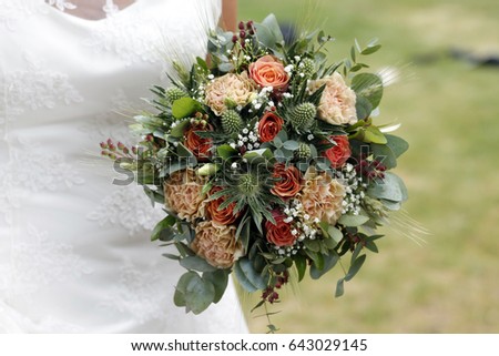 Close-up of bridal bouquet with coral roses, peach peonies and green thistle eryngium