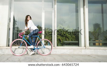 stylish modern hipster girl  sit on sport vintage bicycle against window with plants background of the building. Cute brunette woman think about something