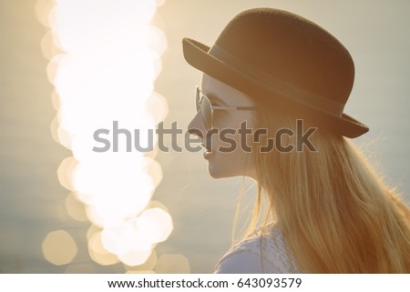 Portrait of young pretty woman wearing hat and sunglasses outdoor on sunset
