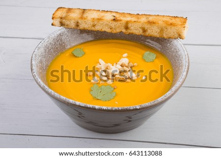 Bowl of pumpkin soup with nuts on wooden board