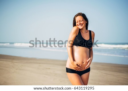 Portrait of beautiful happy dark-hear pregnant woman in black bikini on the beach