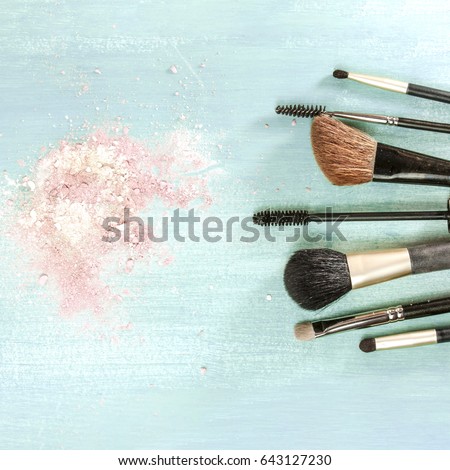 Makeup brushes on a teal blue background, with traces of powder on it. A square template for a makeup artist's business card or flyer design, with plenty of copyspace