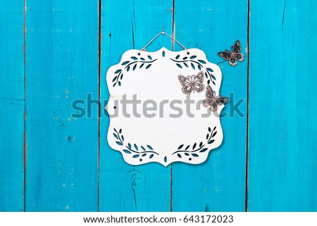 Blank wood sign with floral border and butterflies hanging on antique rustic teal blue wooden door; family, home, love concept background with white copy space
