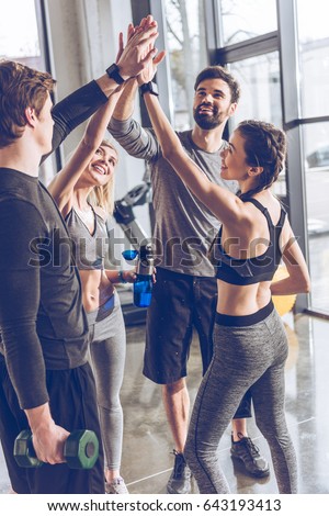 Happy young athletic people in sportswear giving high five in gym Royalty-Free Stock Photo #643193413