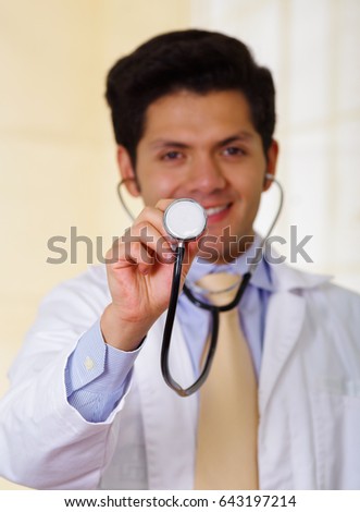 Close up of a confident handsome smiling doctor using Stethoscope, in office background