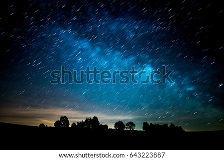Silhouette of the horizon at night. Trees and the Milky Way dominates the photo. Longer exposure, star trails.