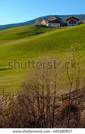 Spring in the Dolomites. A view of the houses standing on the green slopes of the mountain. The old church in the village of Santa Madalena.