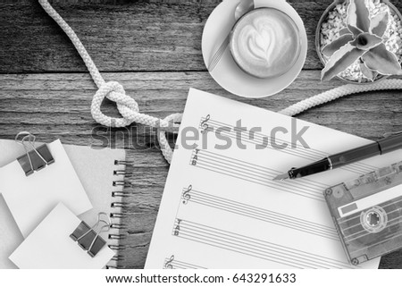 Sheet music, cactus, fountain pen, tape cassette and coffee latte on vintage wooden table, black and white style