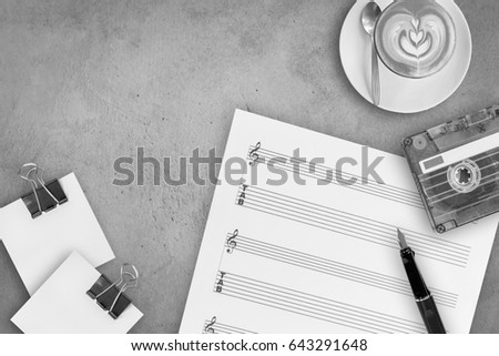 Sheet music, fountain pen, tape cassette and coffee latte on wooden table, top view picture, black and white style