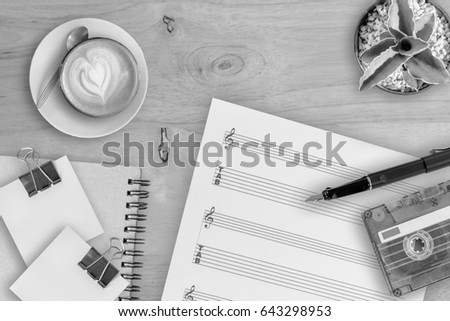 Sheet music, cactus, fountain pen, tape cassette and coffee latte on wooden table, top view picture, black and white style