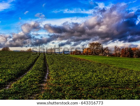 Scenic fine art impressionistic color panorama image of a rural idyllic countryside landscape in Frankfurt am Main, Germany, in vintage painting style, field,tree,blue sky,cloud,church tower,tracks