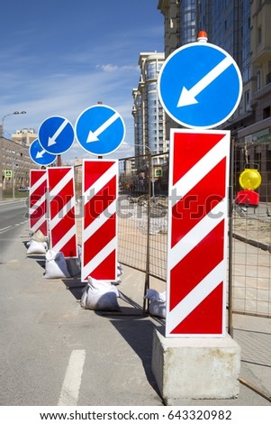 Row of road signs. White arrows on blue background. Way for vehicles. City street and houses in  the background