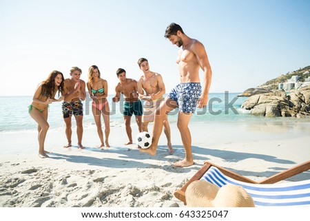 Full length of happy friends looking at man balancing soccer ball on shore