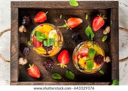 Vegan dietary food. Vitamins. Summer dessert, Salad of fresh organic fruits - mango, peach, apple, banana, kiwi, strawberry, blackberries. In glasses, white table in wooden tray. copy space  top view