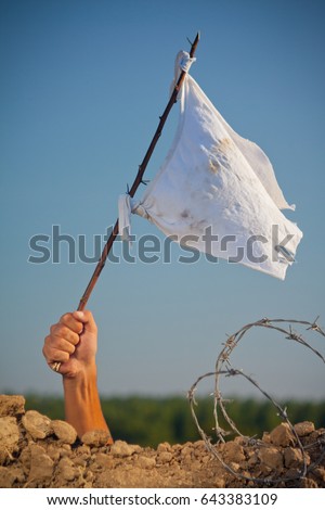 Arm holding stick with a white flag. Soldier in trench with barbed wire surrendering in war battle. Royalty-Free Stock Photo #643383109