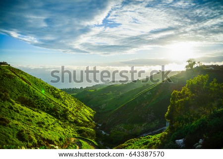 Small valley leading to the sea with green hills and blue cloudy sky.