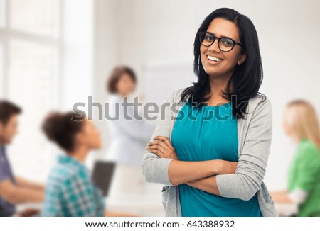 education, high school and people concept - happy smiling young indian woman or teacher in glasses over classroom background Royalty-Free Stock Photo #643388932