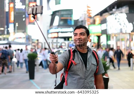 Handsome smart tourist using a selfie stick in urban city location 