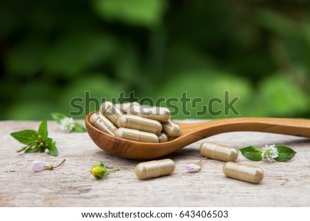 Pile of herbal capsules on wooden spoon with herbs and green natural background  Royalty-Free Stock Photo #643406503