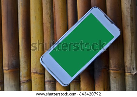 White cellphone with green display on bamboo background
