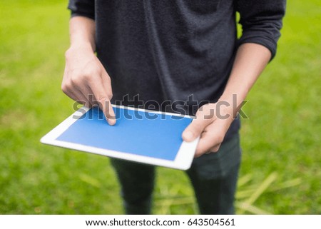 Man uing mock-up digital tablet with blue screen on green background.