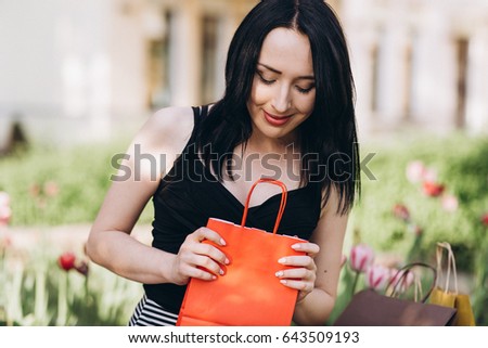 Fashionably dressed woman with colored shopping bags sitting near flowers on the streets, shopping concept