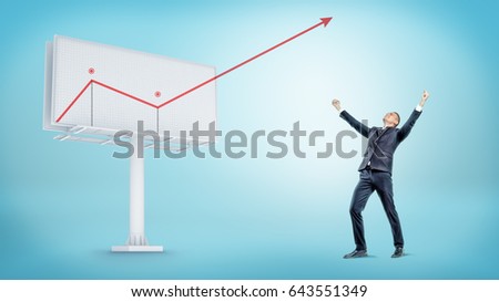 A happy businessman standing beside a large billboard with a red statistic arrow jumping out of it. Incredible profit. Unexpected income. Revenue report.