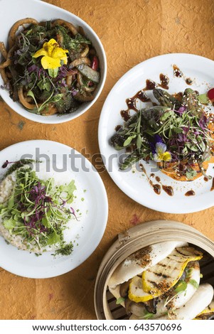 Overhead shot of vegetarian dishes including stir-fried noodles, rice, salad, and Chinese buns
