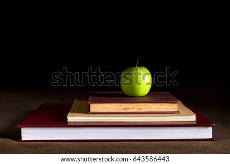 Close up of books and green apple on dark background , Green apple resting on the books , learning objects education concept 