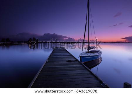 Sailboat at a wooden platform in early morning in a calm lake under a red and blue sunrise