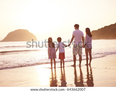 asian family with two children enjoying sunrise on beach.