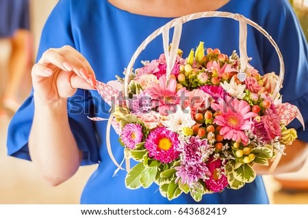Young and elegant woman holding a flower basket with asters and gerberas in her hands.