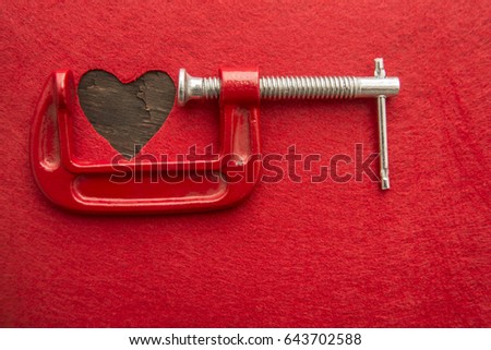 Vise Grip and red heart, concept of stress, sadness, heart broken, Pain. Small red wooden heart under pressure with new vise grip on red material background
