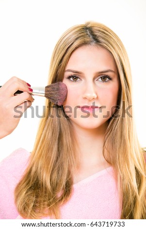 Pink blusher being applied to contour a cheek of a pretty young blond woman using a large soft bristle cosmetics brush in a beauty and fashion concept isolated on white
