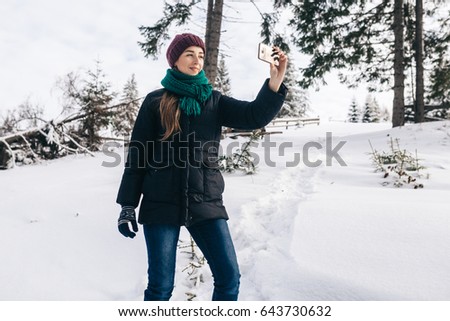 The attractive girl takes a selfie during a winter time. On her a blue jacket, a lilac cap and a menthol scarf. The girl perfectly smiles.