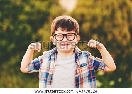 Strong, smart and funny little boy playing outdoors, wearing eyeglasses and blue plaid shirt Royalty-Free Stock Photo #643798324