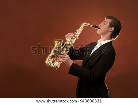 Young man playing saxophone against orange background